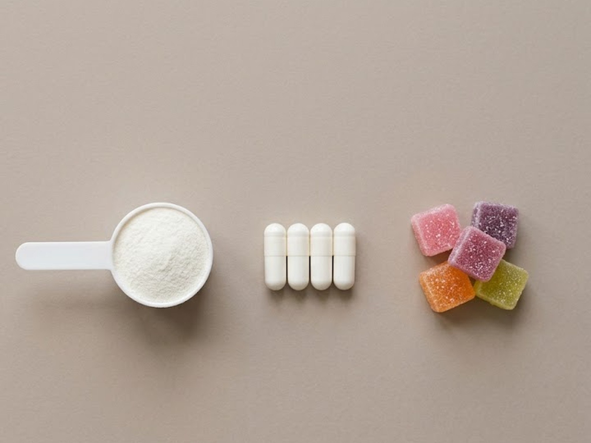 Illustration: a white scoop of fine white powder, four white capsules and five sugar-coated gummies in pink, purple, orange and green, set in a row on plain taupe paper