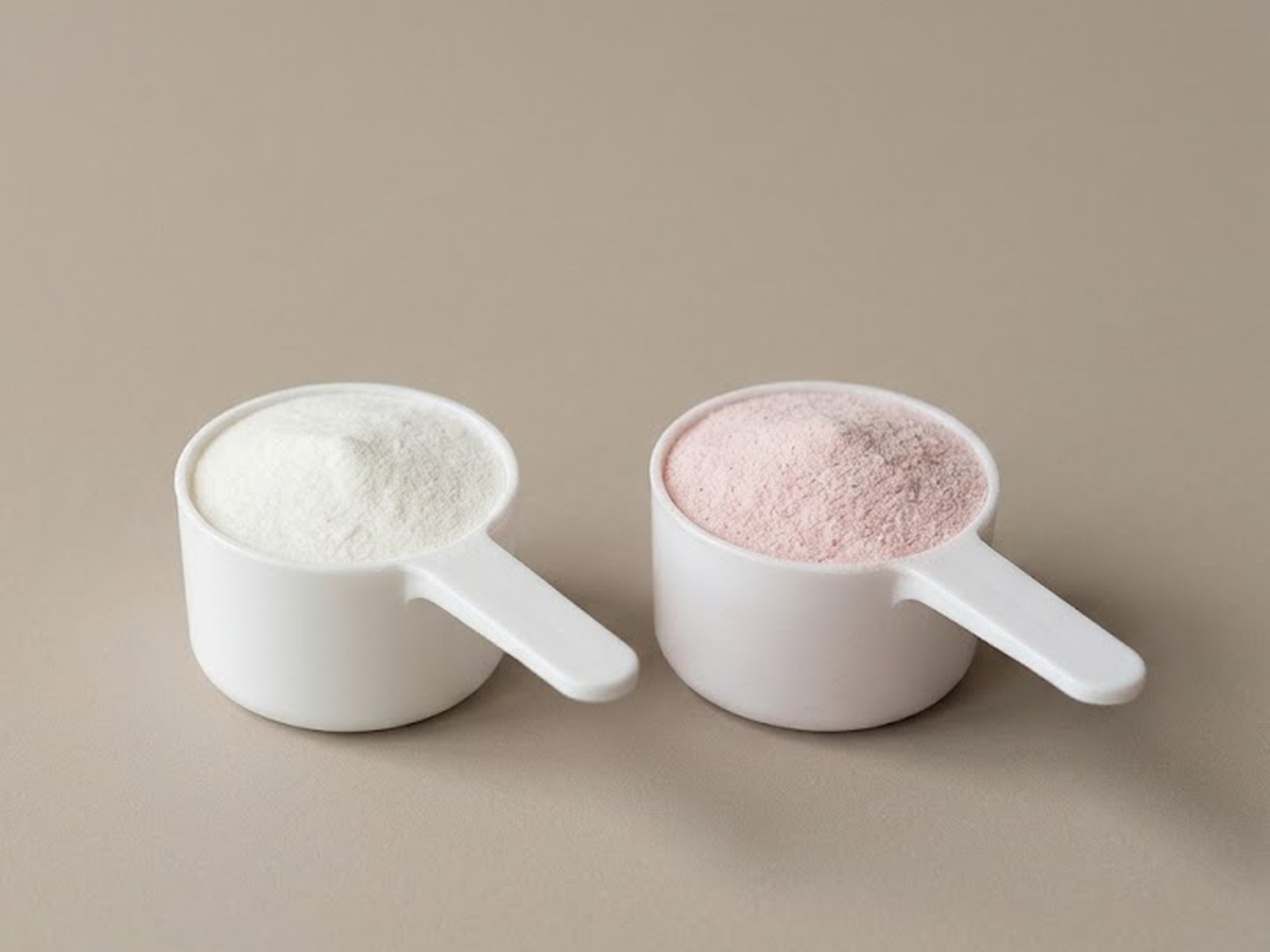 Illustration: two identical white measuring scoops side by side on plain taupe paper, the left filled with plain white powder and the right with pale pink powder
