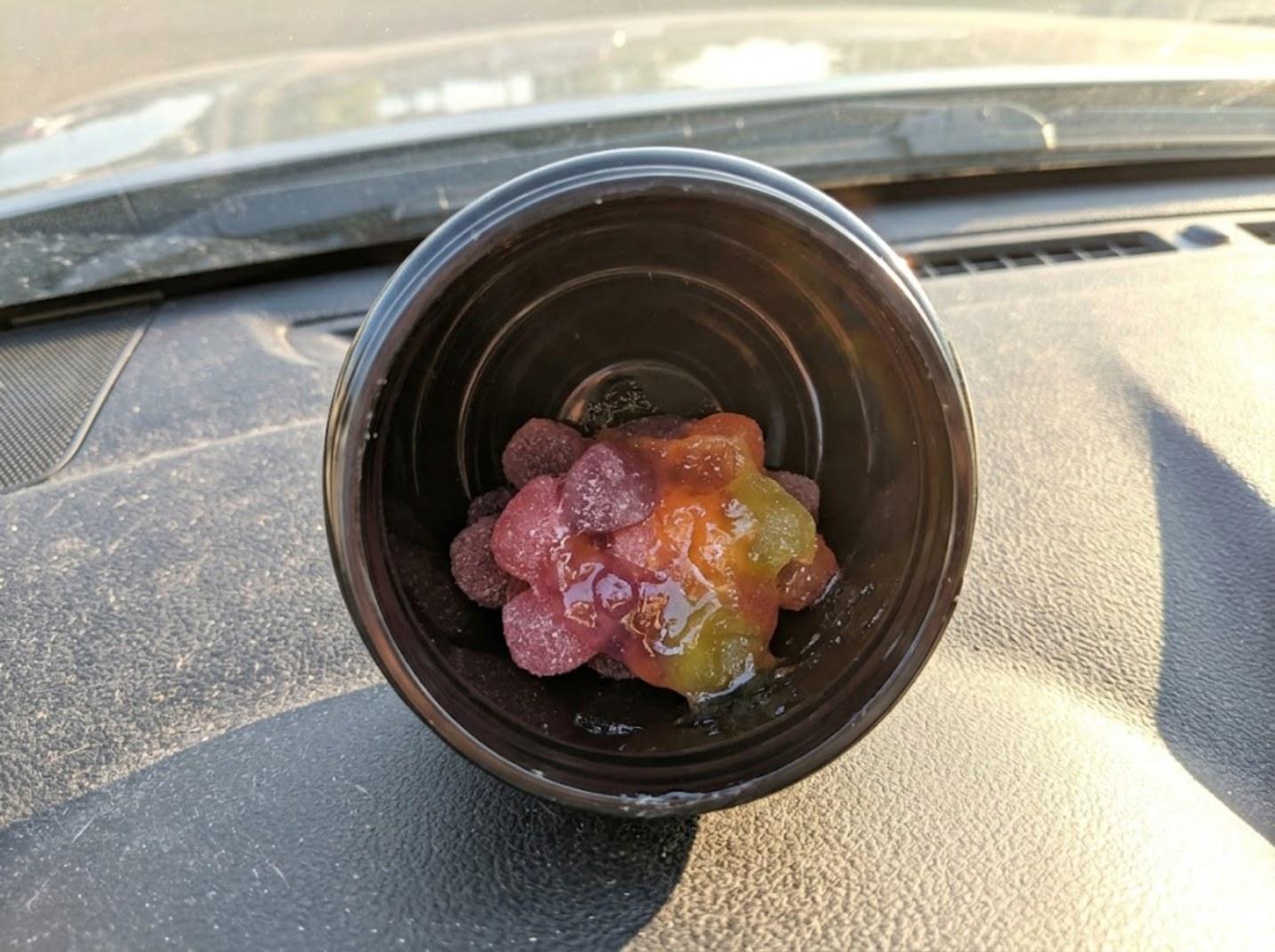 Gummies melted into one sticky clump inside an open tub on a sunny car dashboard